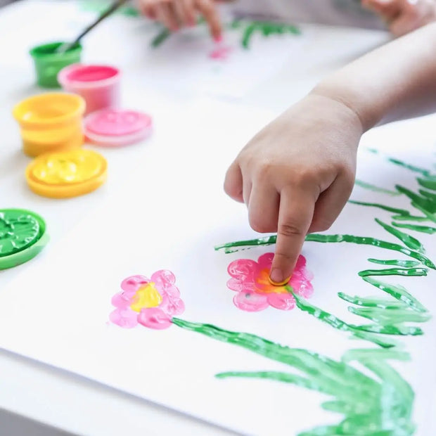 ein Finger eines Kindes malt mit Fingerfarben ab 2 Jahren ein Bild auf einem Blatt Papier